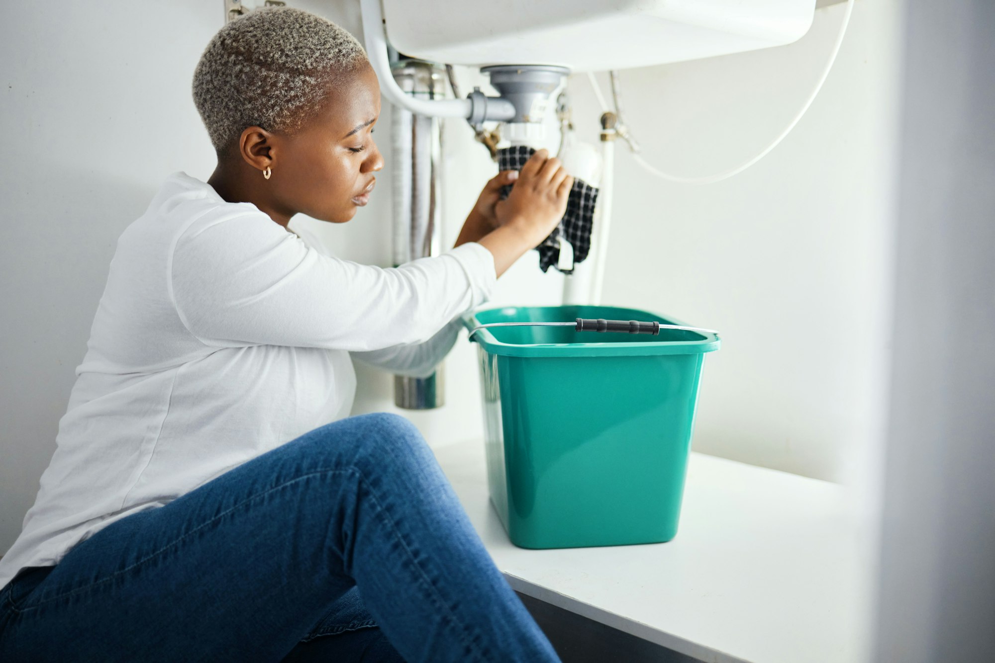 Plumbing, leak and a black woman in the bathroom of her home with a cloth and bucket waiting for as